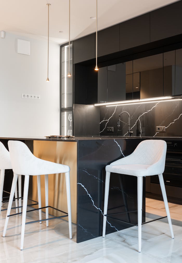 Interior of contemporary kitchen with white chairs at island counter in kitchen with black cabinets in modern apartment